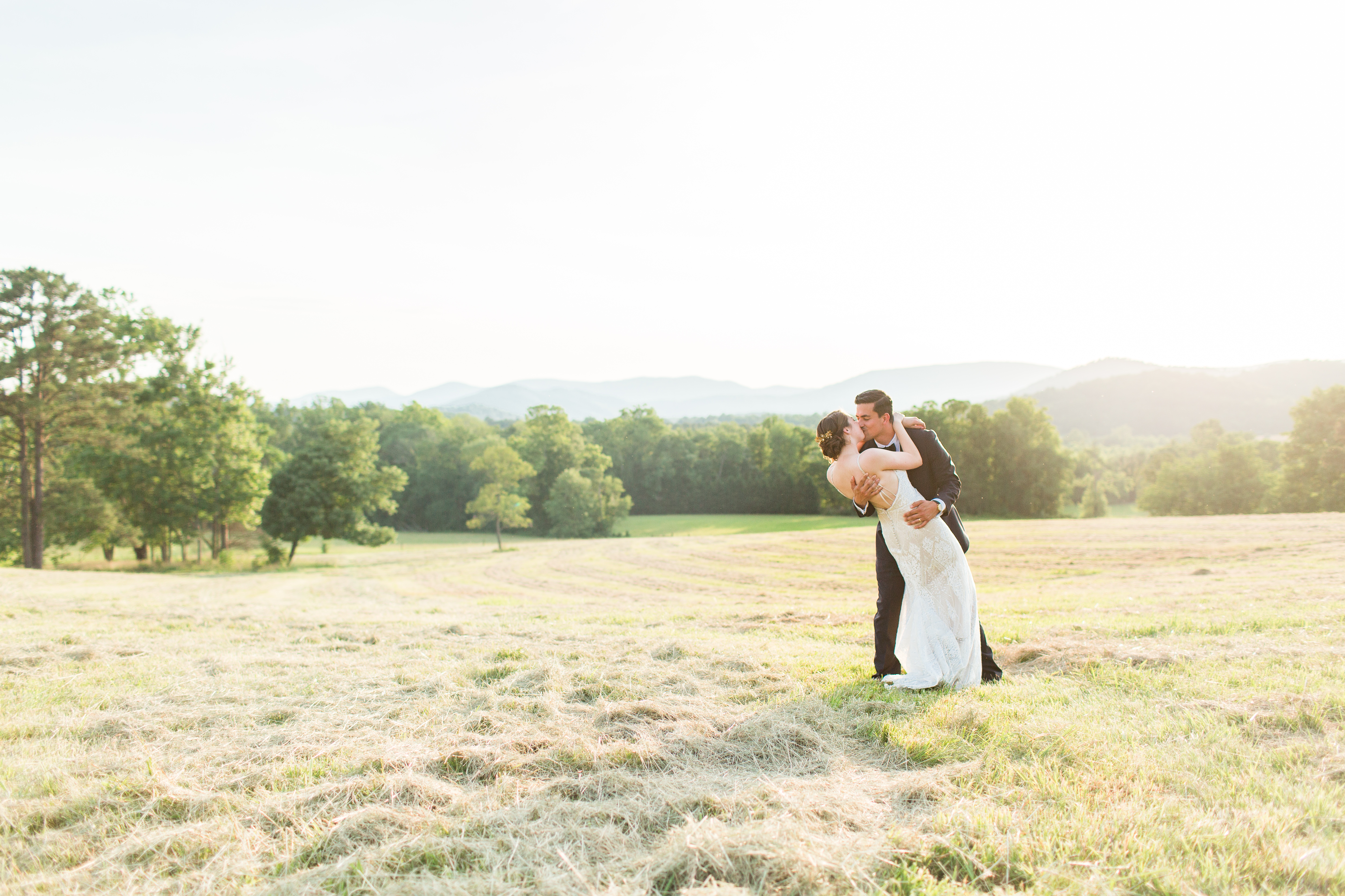Bride and Groom kissing in a country field at sunset. Mountain skyline 